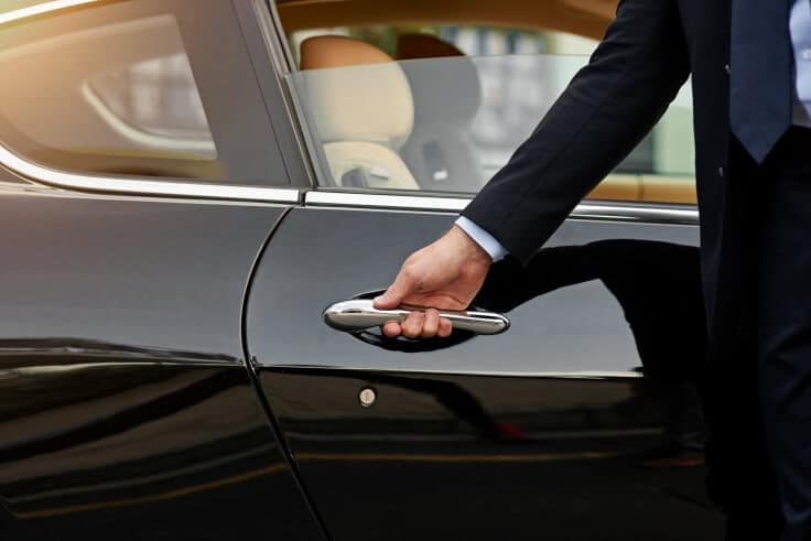 Professional chauffeur opening a luxury car door for a passenger during an airport transfer Bristol service.
