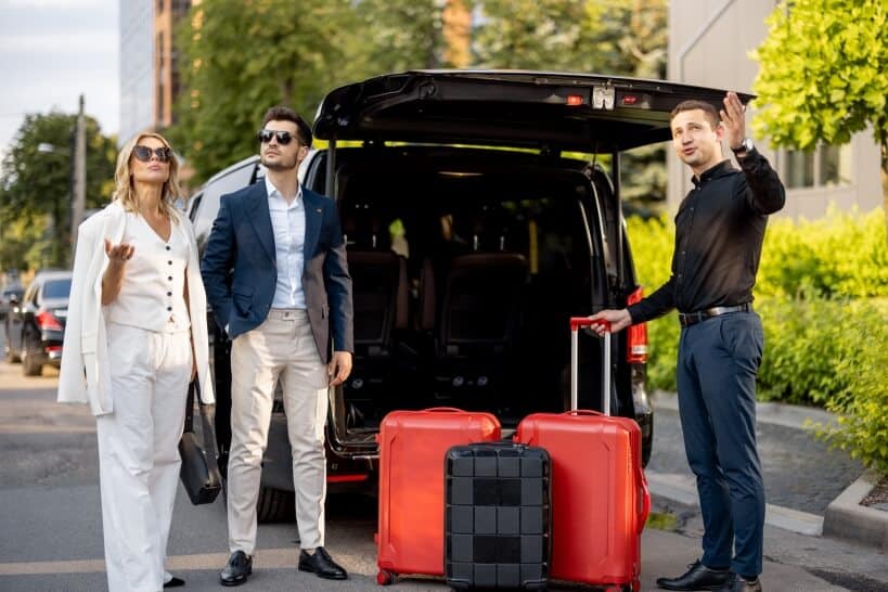Professional chauffeur assisting two stylish travelers with luggage beside a luxury vehicle for reliable airport transfers Bristol service.